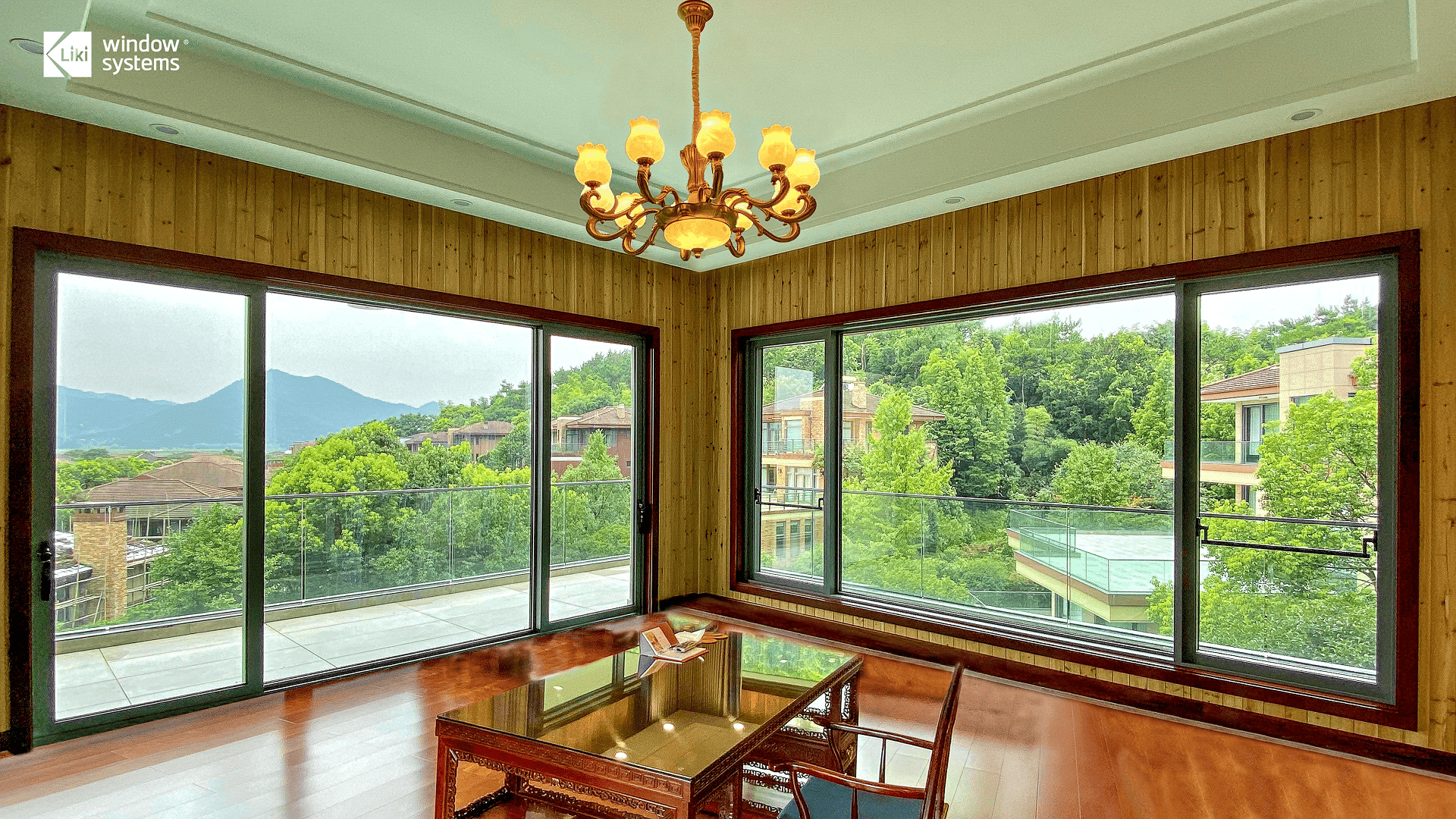Spacious living area with warm wood interiors and expansive LIKI aluminum sliding glass doors, creating a seamless transition to the lush green outdoors.