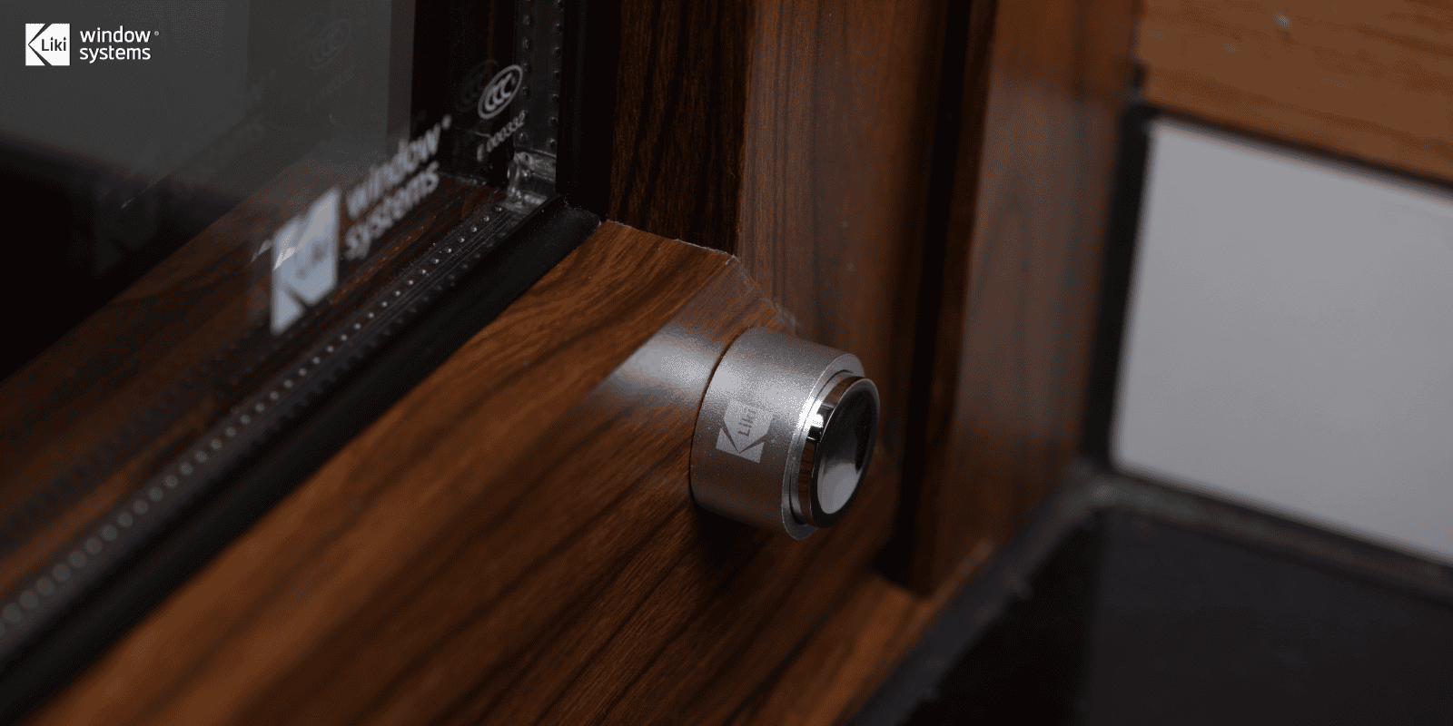 LIKI branded custom security hardware component integrated into a wood-finish aluminum window frame, showcasing attention to detail.