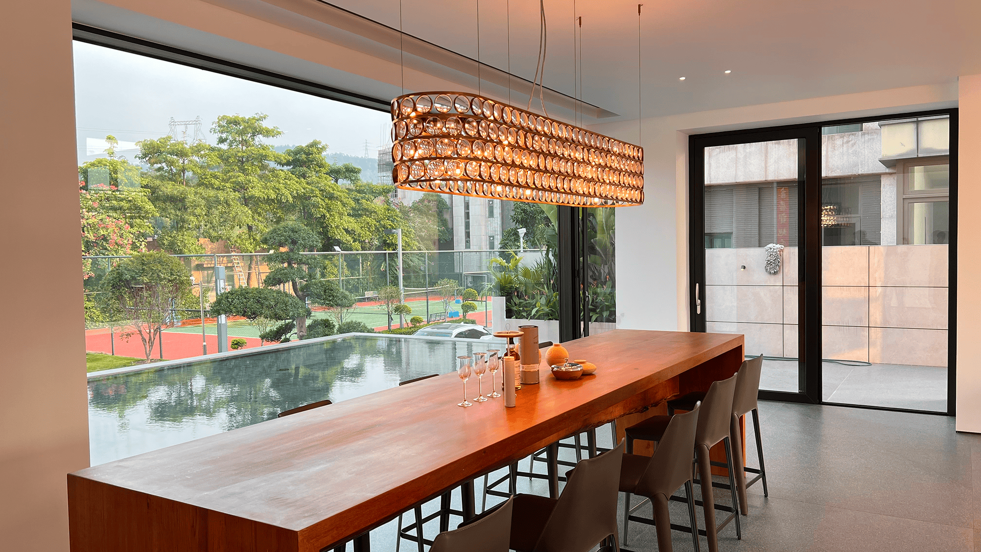 Modern luxury dining room featuring a combination of LIKI large fixed picture windows overlooking a pool and a side hinged aluminum door for patio access, showcasing a complete architectural glazing solution.
