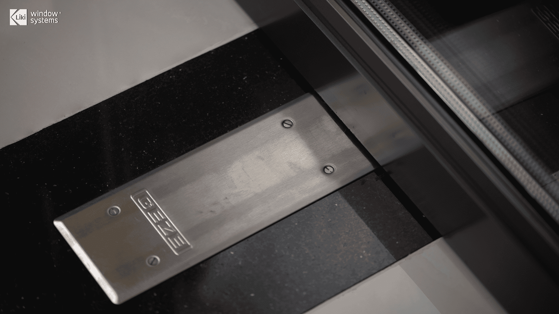 Detail shot of stainless steel GEZE floor hardware integrated into a LIKI architectural door system, showcasing the global supply chain integration.