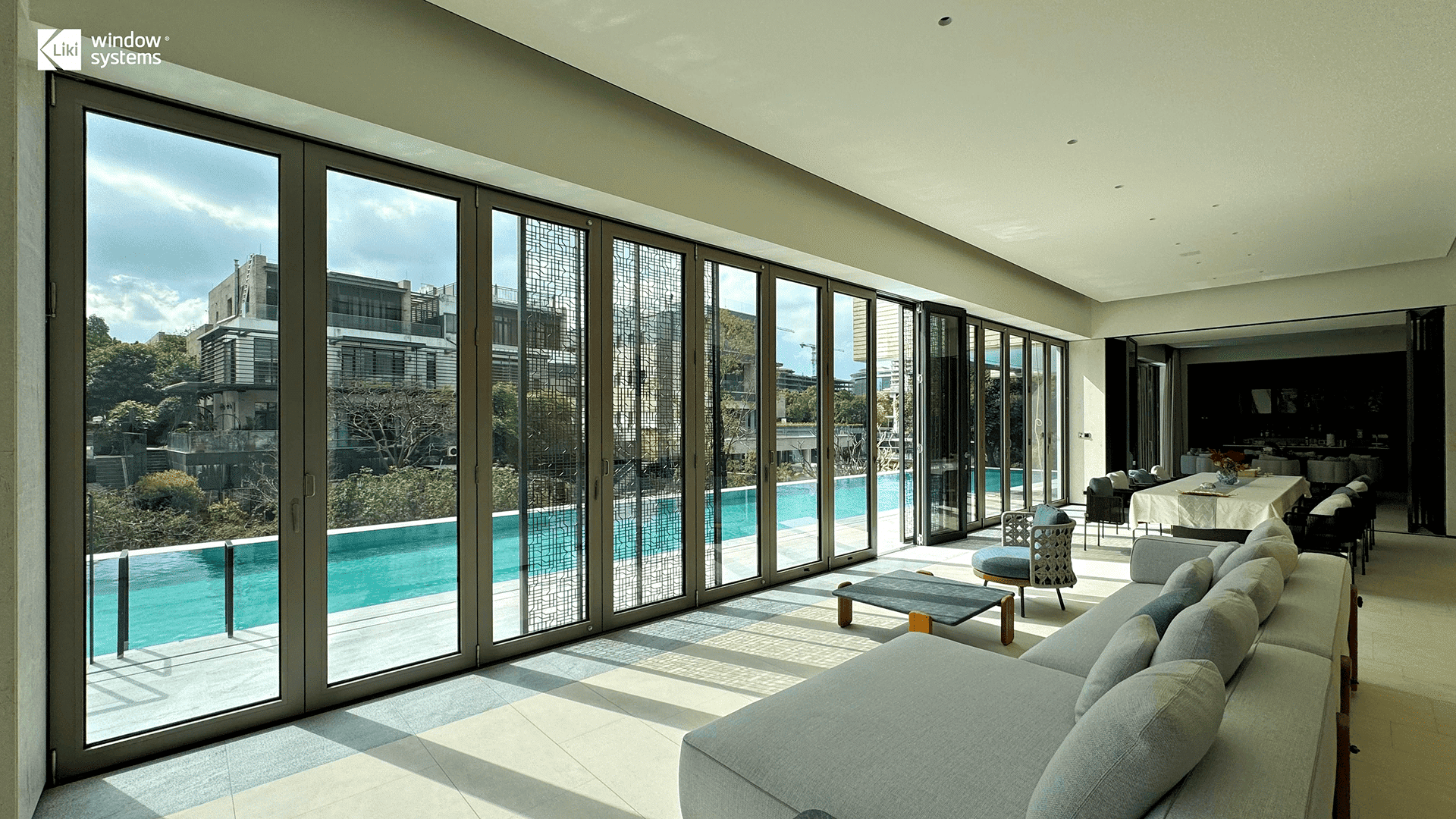 Expansive LIKI aluminum bi-fold door system featuring custom grid design, connecting a luxury living room to a swimming pool patio, demonstrating large-span architectural capabilities.