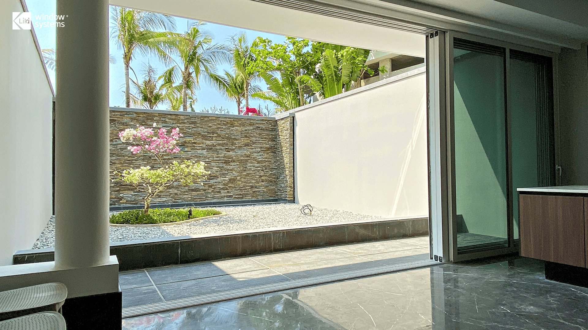 LIKI multi-track aluminum sliding glass door with a flush threshold, offering seamless indoor-outdoor flow to a private courtyard garden.