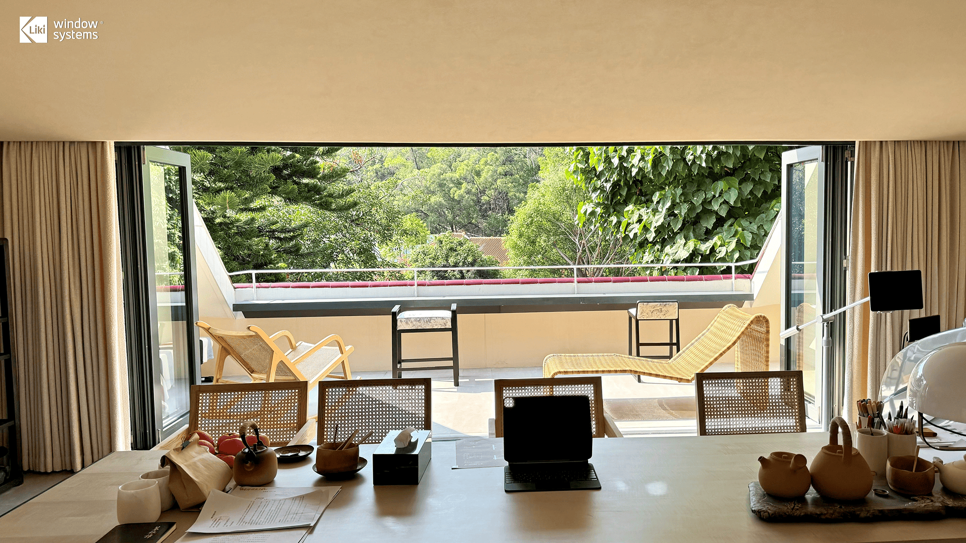 Interior view looking out through a fully opened LIKI bi-fold door system, demonstrating how folding glass walls maximize natural light and merge indoor dining spaces with the outdoors.