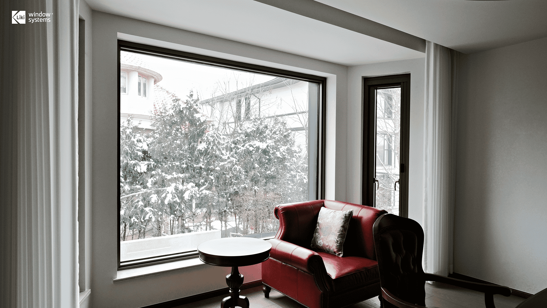 Cozy living room with large LIKI thermal break aluminum picture window overlooking a snowy winter landscape, demonstrating superior insulation and energy efficiency.