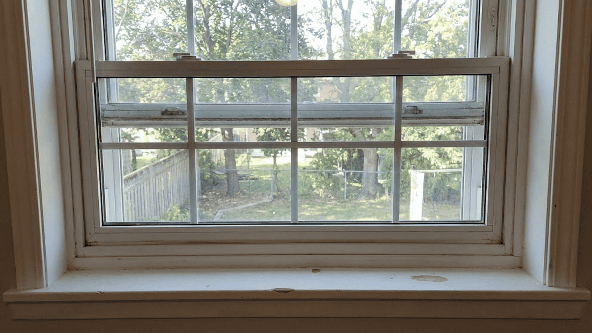 Traditional vinyl double-hung window with thick frames and grid patterns, illustrating the visual obstruction compared to modern slim aluminum windows.