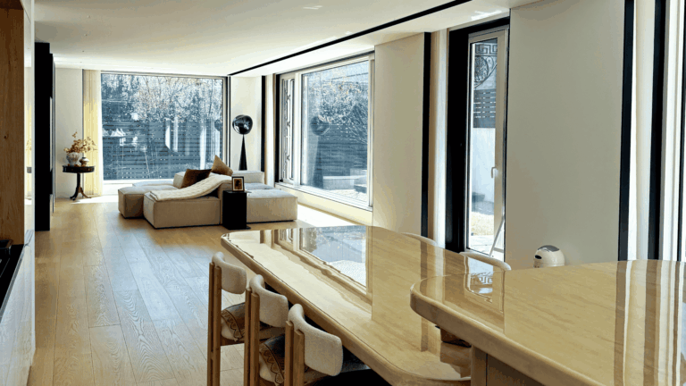 Spacious great room featuring floor-to-ceiling parallel opening windows that capture passive solar heat, contrasting the warm interior with the bare winter landscape outside.